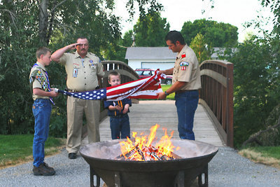 Image: Scoutmaster Ron Gilman of Smithfield salutes the flag as three Hyrum scouts prepare the flag for disposal.